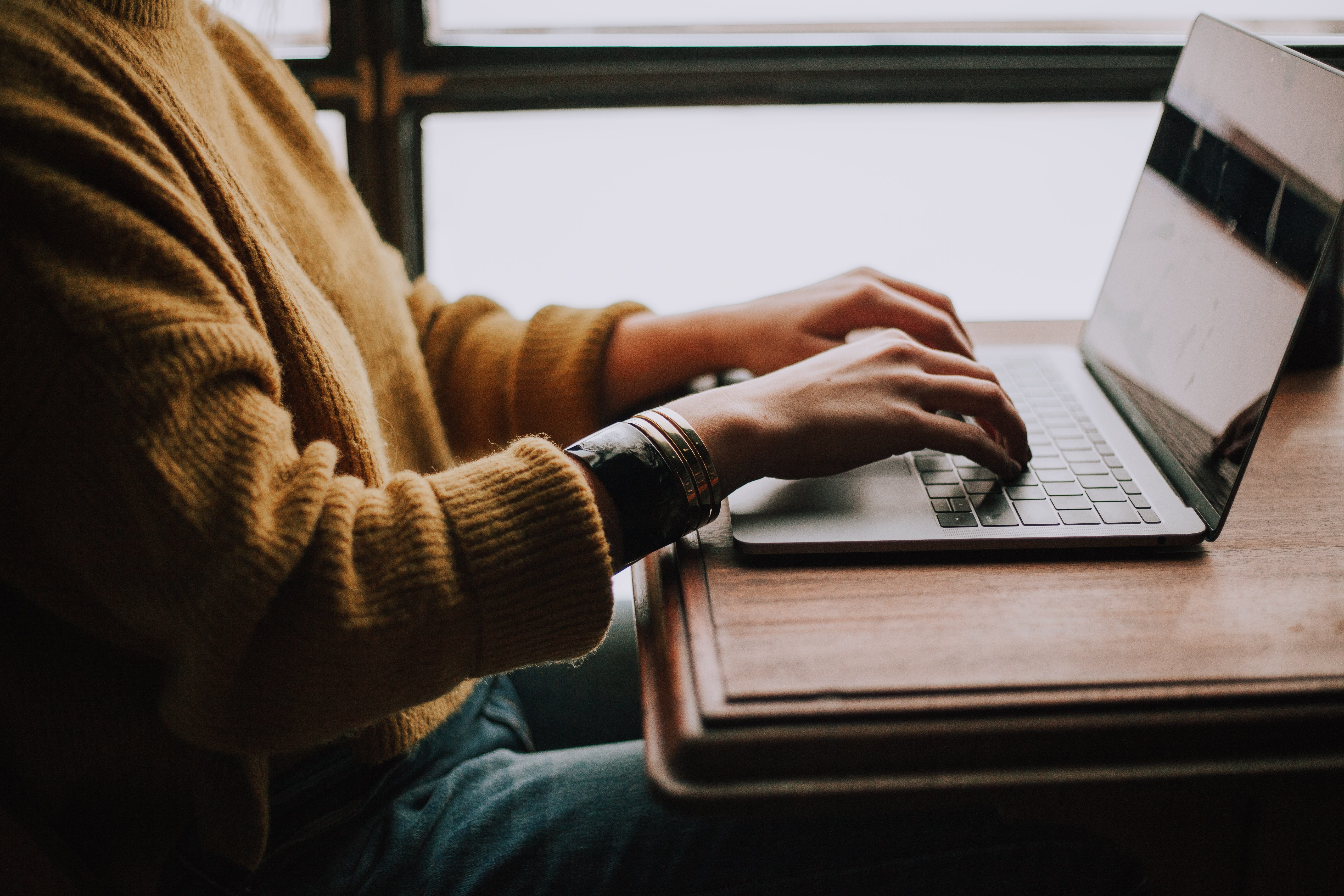 person with yellow jumper typing on a laptop