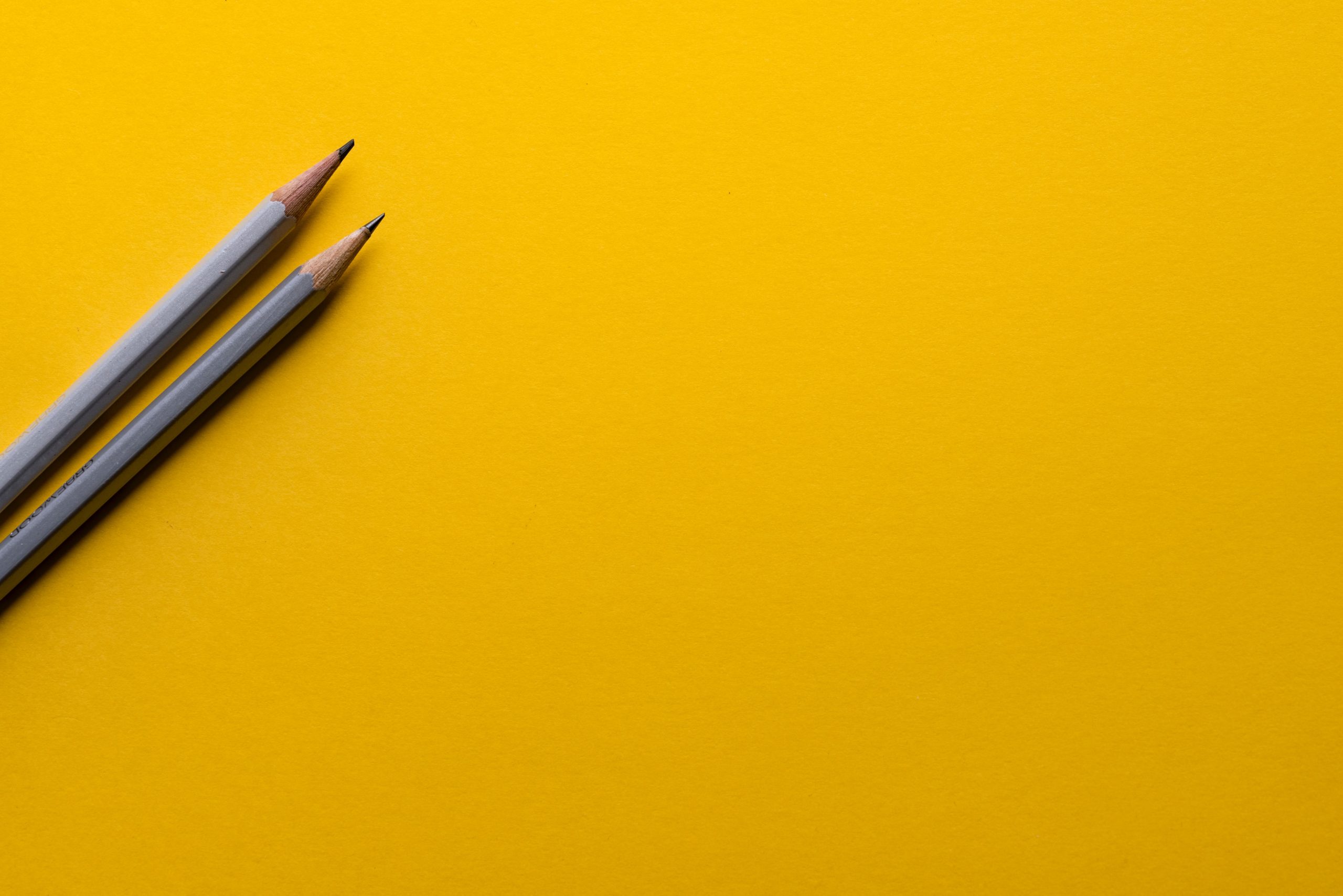 Two pencils against a yellow background