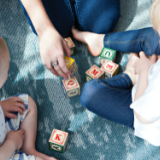 Parent playing a letter block game with two toddlers