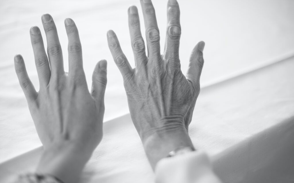 Black and White image of two hands outstretched. The hand on the left is youthful and the hand on the right is wrinkled.