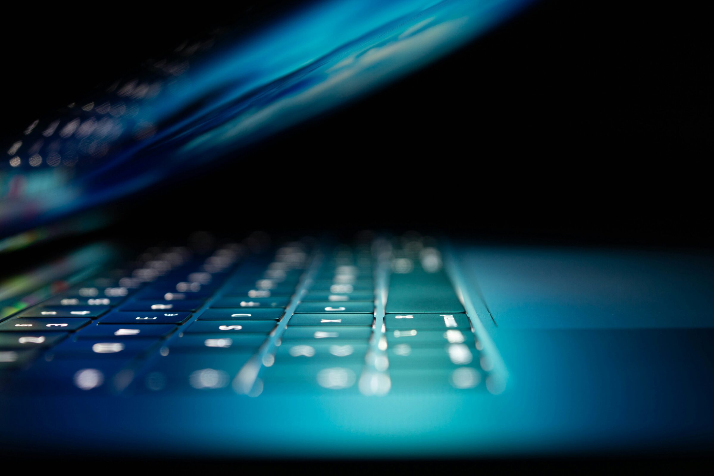 Opened laptop, with light of screen illuminating the keyboard.