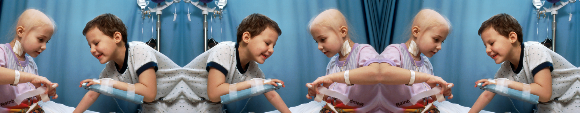 Two child cancer patients playing together on a hospital bed