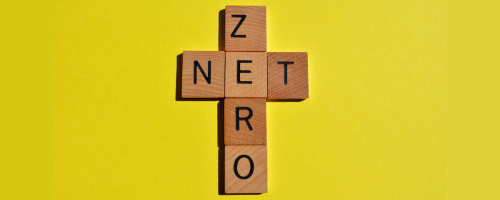 'Net Zero' spelled out in wooden letter blocks. Sits on a yellow background