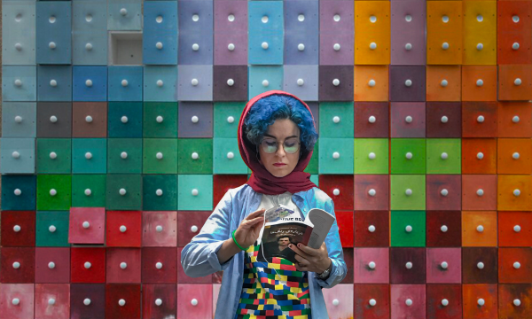 A person holding their mobile phone over a text book with a vibrant coloured background.