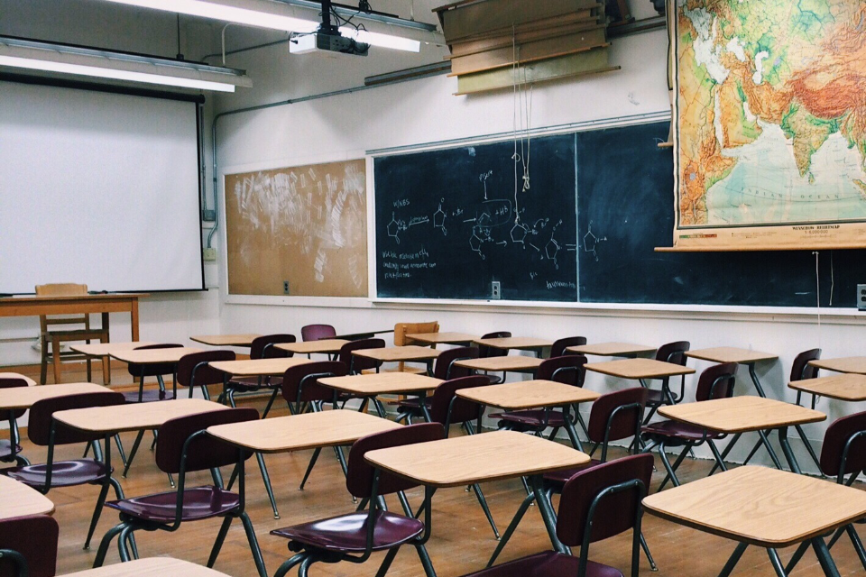 Classroom scene of empty desks with a chalkboards and map on the back wall