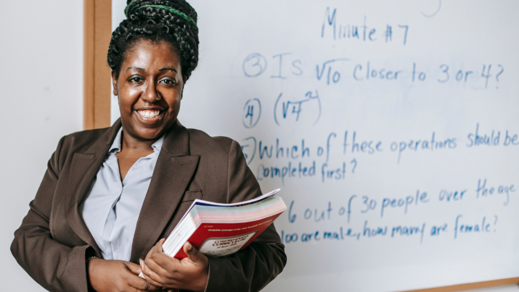 African American Teacher Education Author Wearing a Brown Blazer Holding Research Books in front of an Easel Board