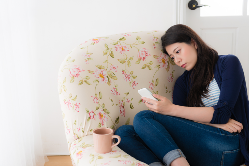 Woman on couch feeling sad on her phone