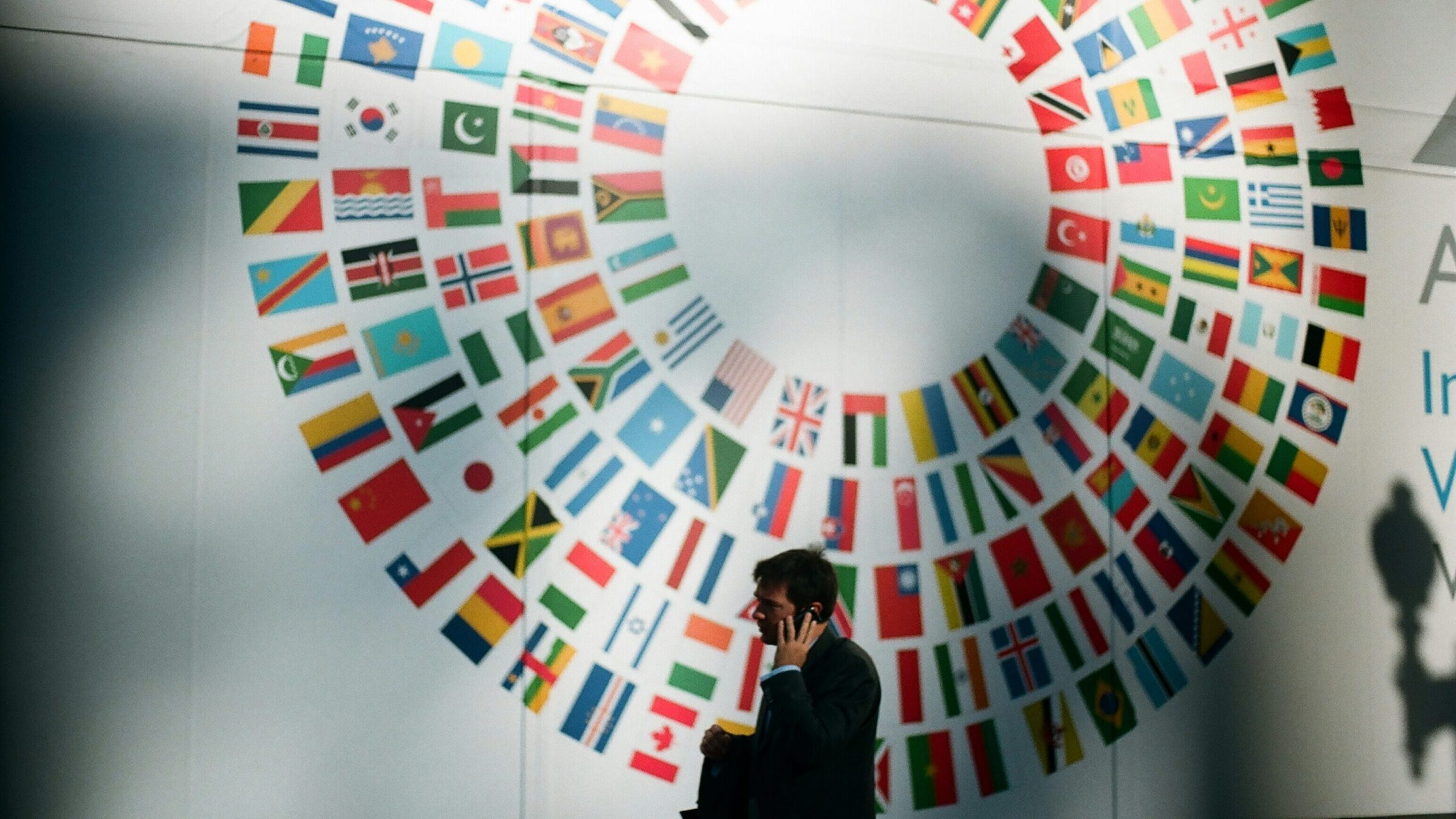 a man answering a call in front of a wall with different countries flag printed on it.
