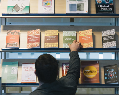 a person standing in front of a book shelf with our books