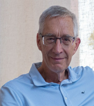 A portrait photo of Professor Stephen L. Esquith, taken of the shoulders upwards against a beige background. Prof. Esquith is wearing a light blue polo shirt with a collar and glasses. They have white and grey hair and white skin.